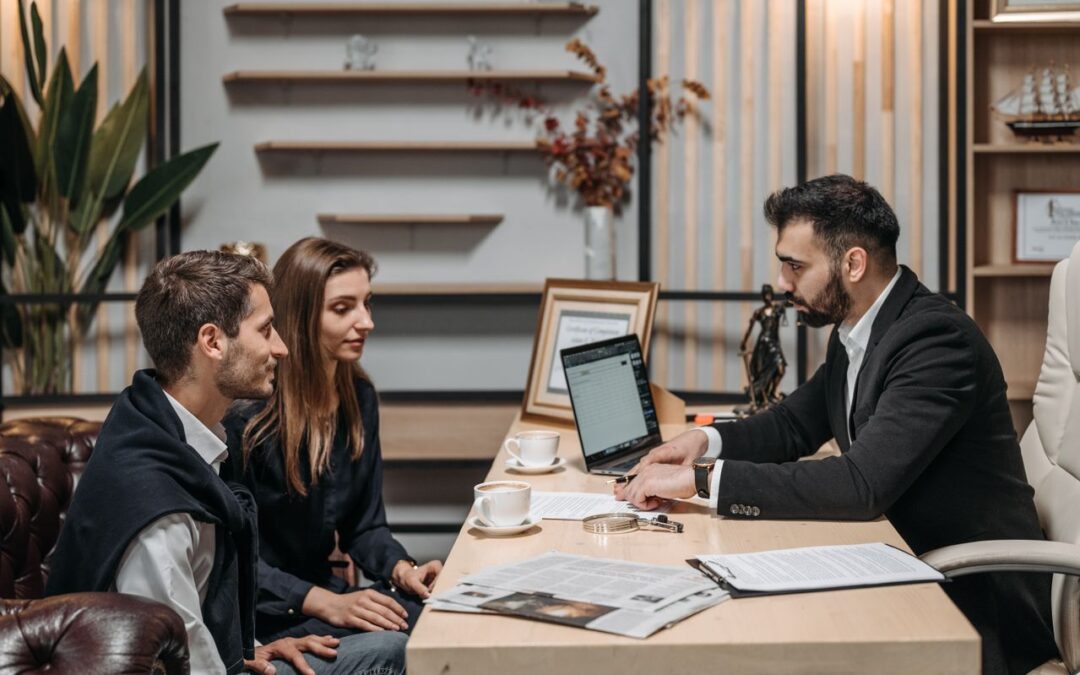 Un conseiller financier en costume échange autour de son bureau avec un jeune couple attentif lors d'un rendez-vous professionnel